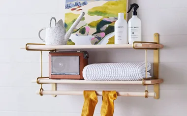 Laundry room with shelf holding artwork, towels, watering can, and bottles; yellow socks hanging below.