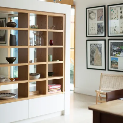 Modern interior with a wooden shelving unit displaying decor and books; framed art on the wall and a wicker chair nearby.