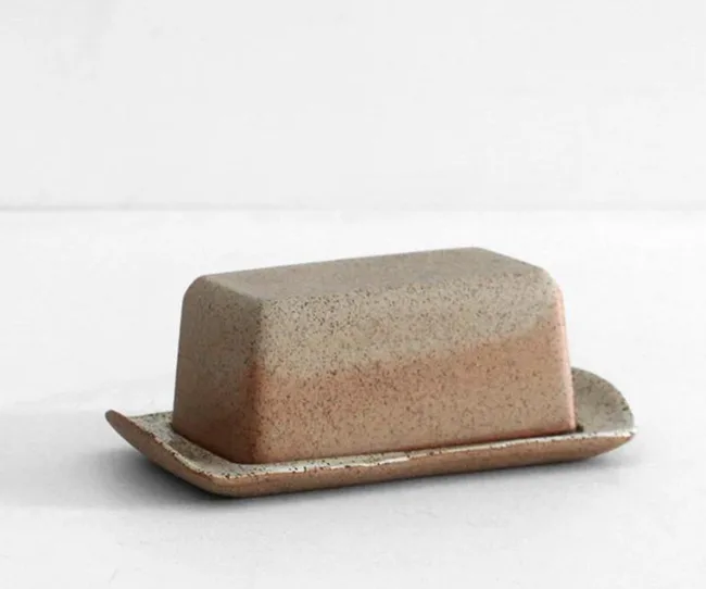 Ceramic speckled butter dish with a lid, resting on a matching tray, set against a light background.