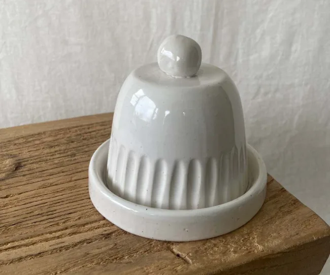 White ceramic butter dome on rustic wooden surface with a neutral background.