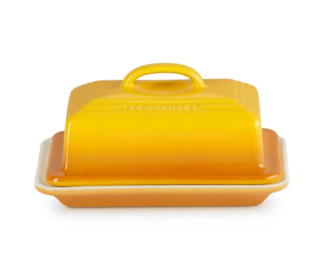 Yellow Le Creuset butter dish with a smooth, gradient finish and a handle on top.