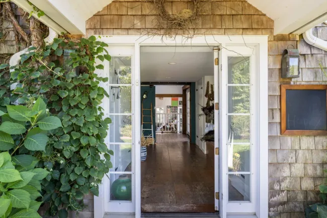 Open wooden door with glass panes, leading to a bright interior hallway with plants outside and a chalkboard on the right.