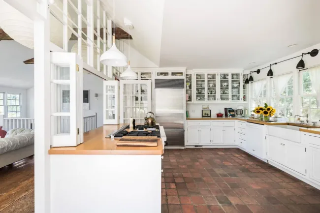 Bright kitchen with white cabinets, stainless fridge, sunflowers on counter, and terracotta tile floor.