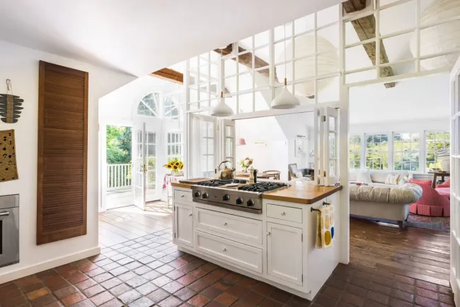 Bright, open kitchen with a central island, tile flooring, and large windows leading to a sunlit room.