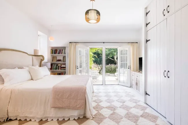 Spacious bedroom with a large bed, open French doors, and a view of a garden.