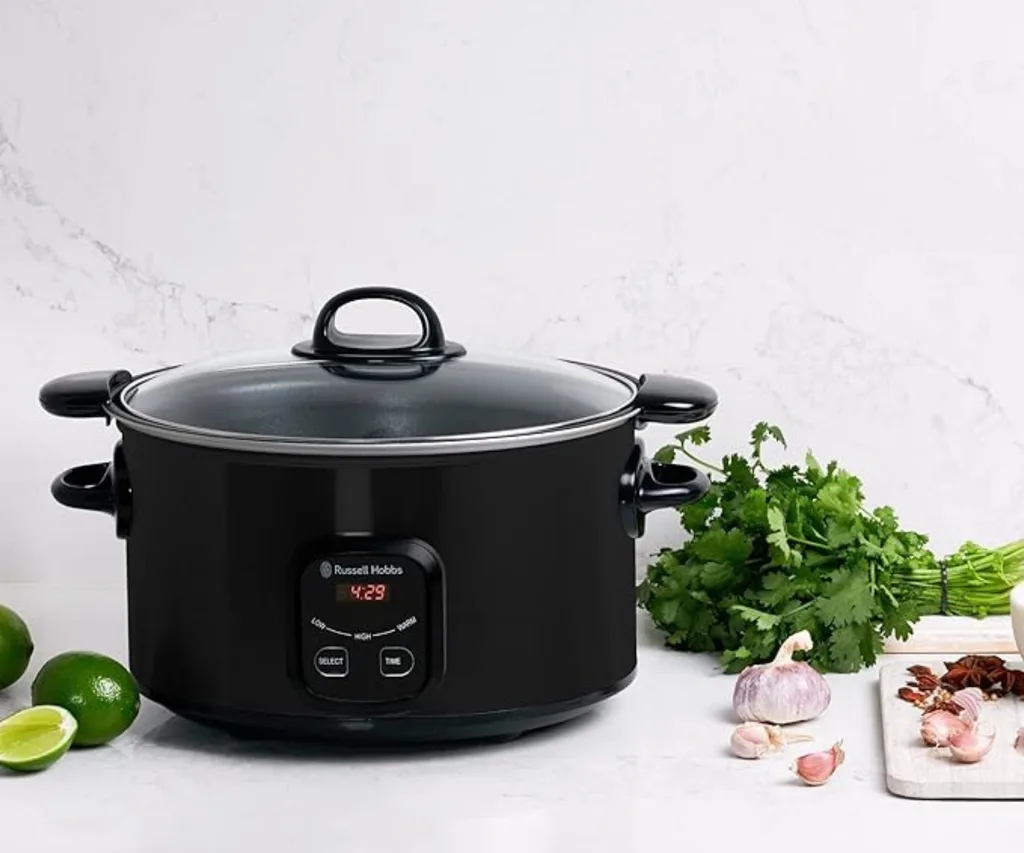 Black Russell Hobbs slow cooker on counter with garlic, herbs, lime, and spices; digital display shows 4:29.