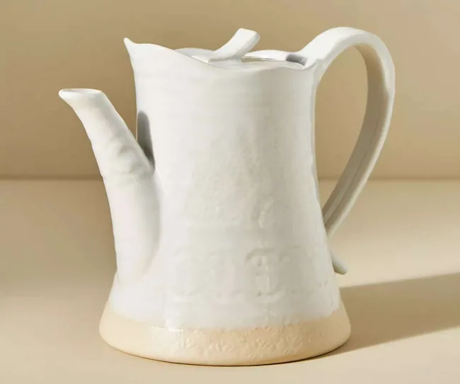 A ceramic white teapot against a yellow background