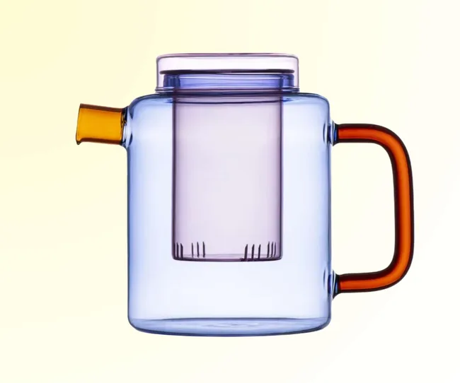 A multi-coloured glass teapot against a yellow background