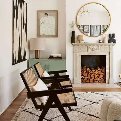 A living room with wood stacked inside the fireplace and a black and white chequered rug on a wooden floor