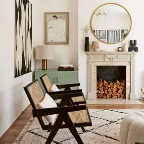 A living room with wood stacked inside the fireplace and a black and white chequered rug on a wooden floor
