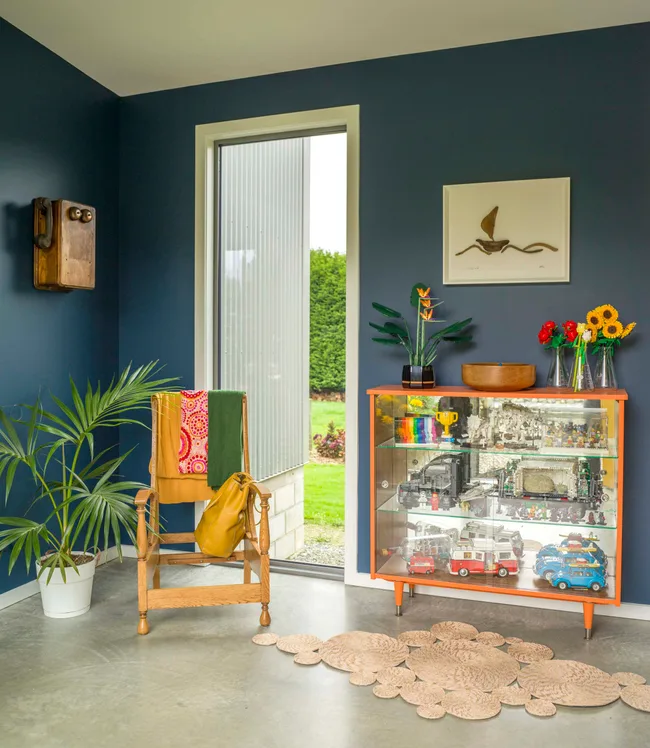 A entryway with navy blue walls, a fluro orange cabinet and a bright yellow chair