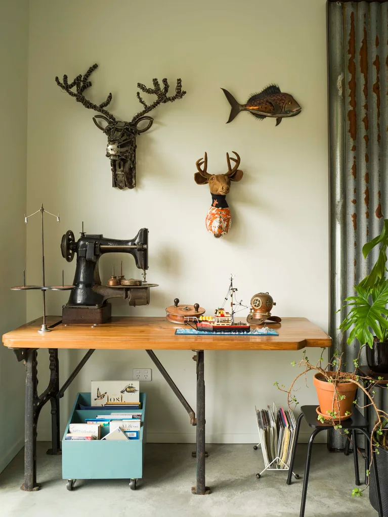 A wooden desk with ceramic and metal deer heads hanging on the cream coloured wall above it