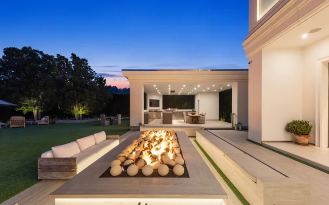 Outdoor seating area with a lit fire pit and modern open-air kitchen under a twilight sky.