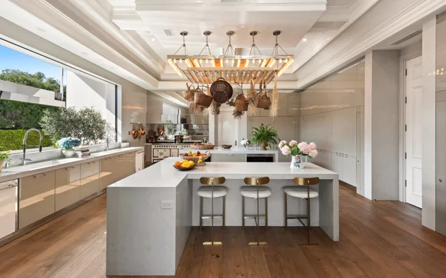 Luxurious kitchen with island, hanging baskets, wooden floor, modern fixtures, and large window with garden view.