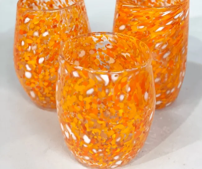 Three orange and white speckled glass cups on a white surface.