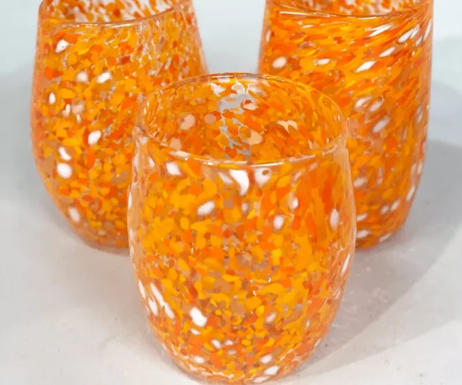 Three orange and white speckled glass cups on a white surface.