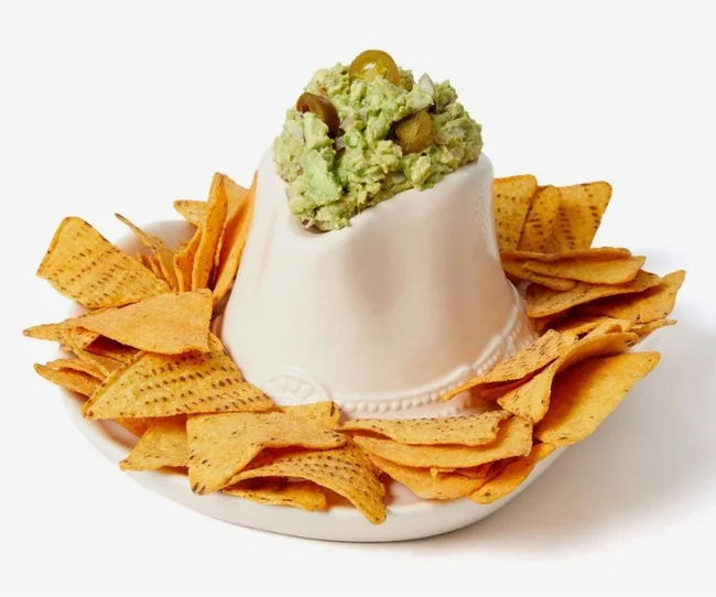 A white ceramic volcano-shaped bowl with guacamole on top, surrounded by tortilla chips.