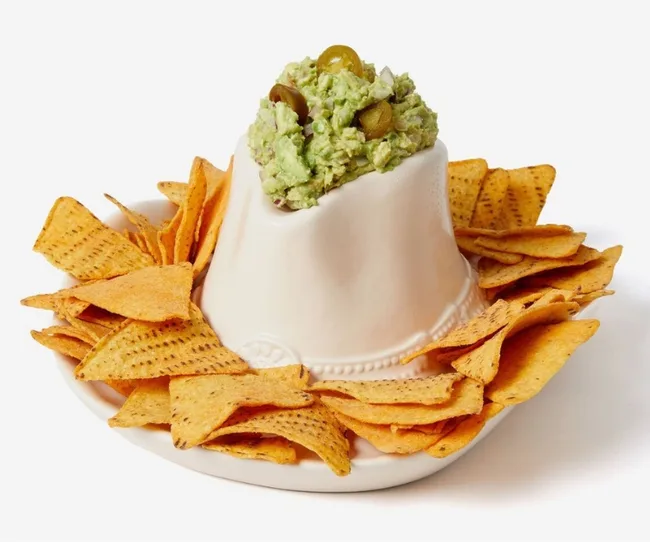 A white ceramic volcano-shaped bowl with guacamole on top, surrounded by tortilla chips.