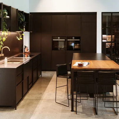 Clean black kitchen furnishings wrapping around the corner of a room, a black and wooden dining room table in the centre