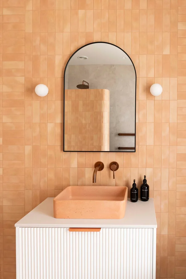 Peach coloured tiles in a bathroom with an oval mirror and white sink