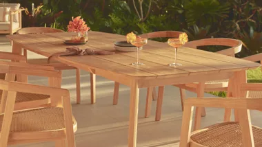 Outdoor wooden dining table set with chairs, two glasses of orange cocktails, and decorative plates.