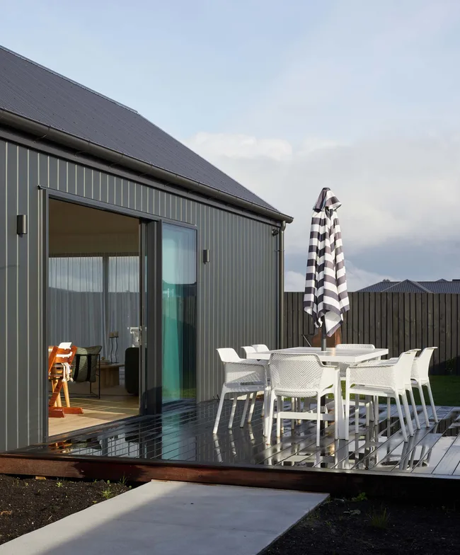 Outdoor patio with white furniture, a striped umbrella, and sliding glass door leading to modern interior space.