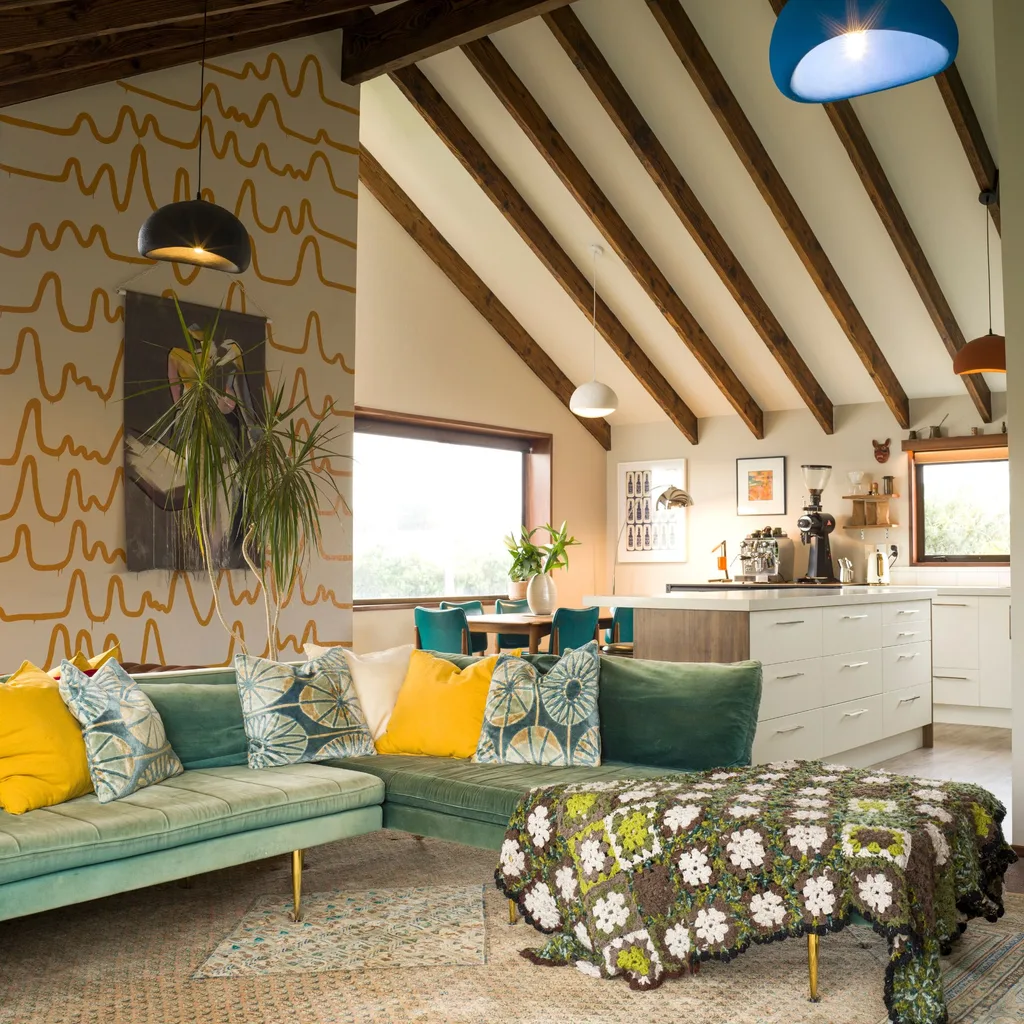 A living room with a yellow squiggly lined pattern on the wallpaper behind the green couch