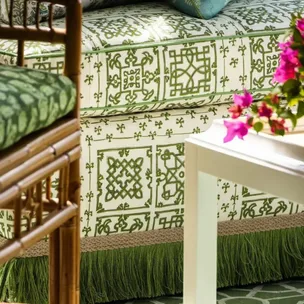 Floral sofa with green and white patterns, a bamboo chair, pink flowers on a table in a cozy living room setting.