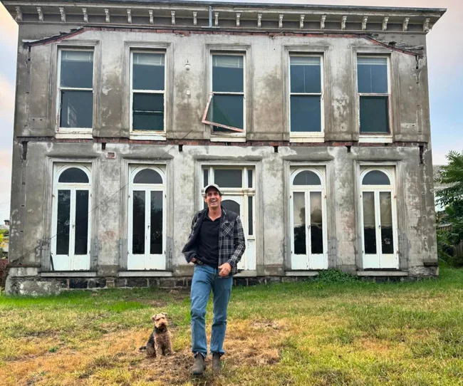 Man and dog standing in front of an old, two-story house with arched windows.