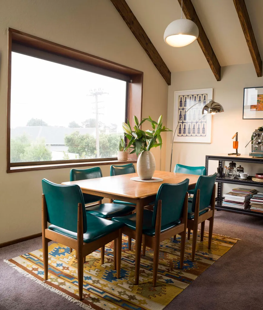 A dining room with green leather chairs around a wooden table, and yellow rug beneath