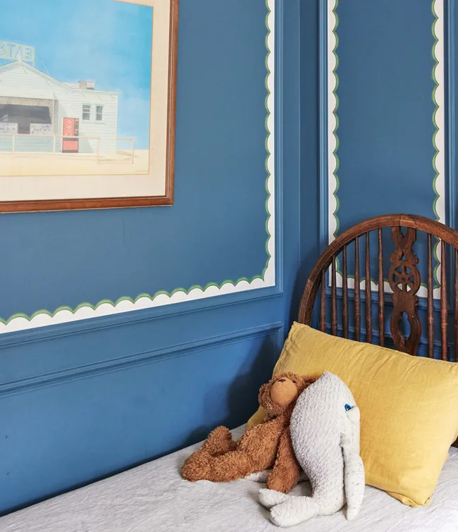 Teddy bear and elephant toy on bed with yellow pillow against blue wall with framed art.