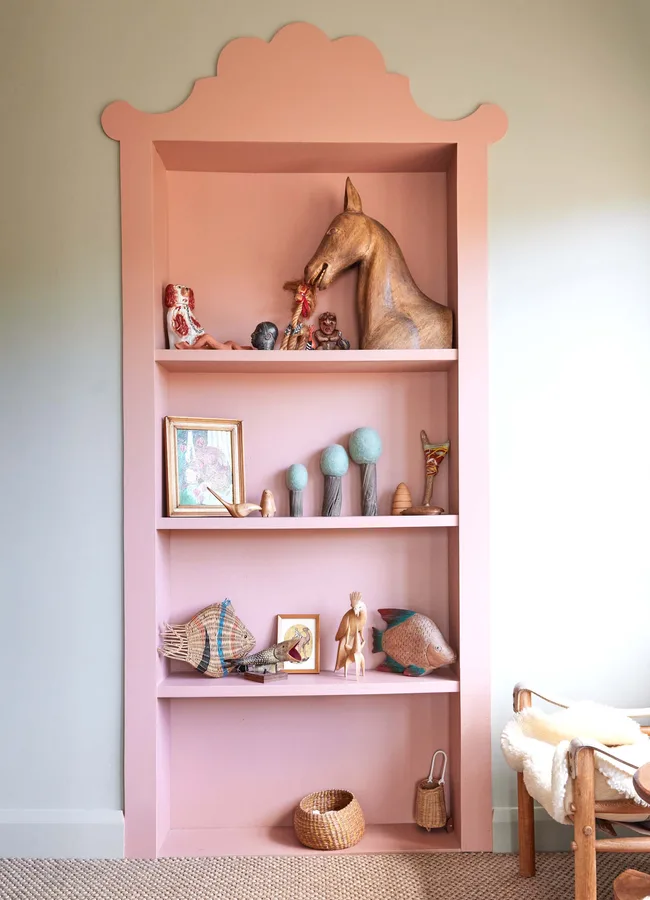A pink shelving unit against a dusty green wall