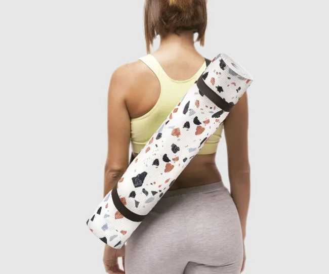 A person in a yellow sports top with a patterned yoga mat on their shoulder, viewed from behind.