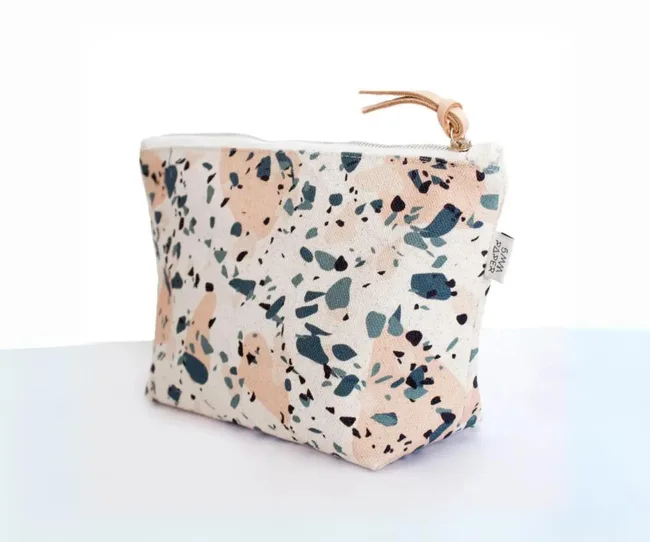 Terrazzo-patterned canvas pouch with zipper and leather pull tab on light background.