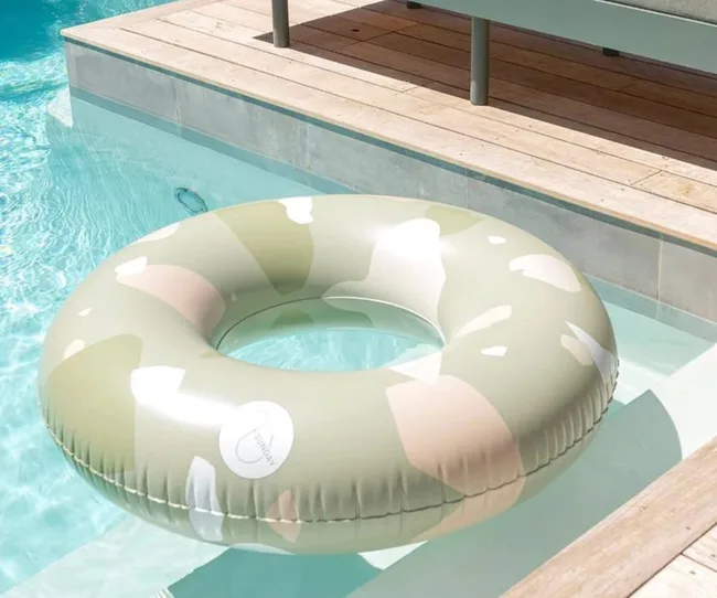 Camouflage-patterned inflatable pool float in clear water by a wooden deck.