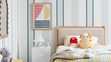 Cozy bedroom with plush toys, striped wallpaper, framed art, and a modern lamp on a white nightstand.