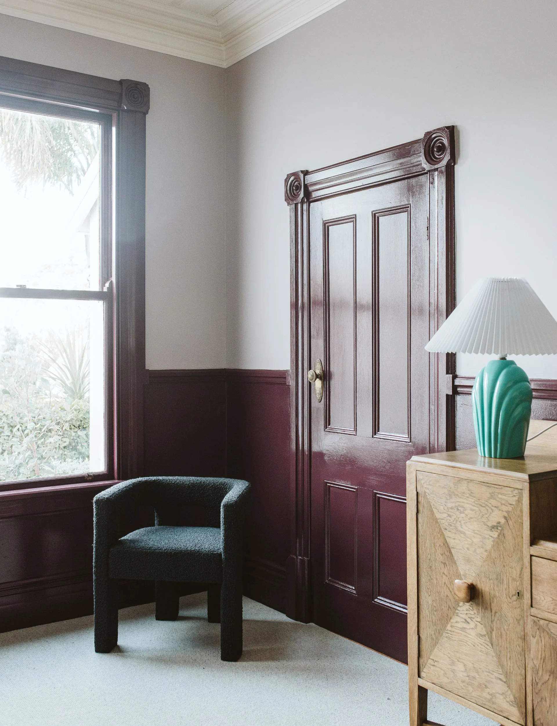 A large maroon door in the New Plymouth villa with a green velvet chair in the corner