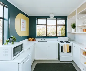 Bright kitchen with white cabinets, stove, microwave, and a large window. Yellow circle wall art and potted plants.