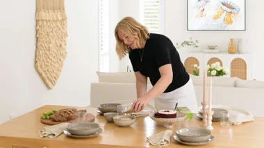 The owner of the Pōhutukawa Coast new-build rearranging dishes on the dining room table