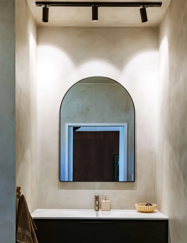 An arch chaped mirror over a dimly lit basin in the Mount Maunganui bungalow