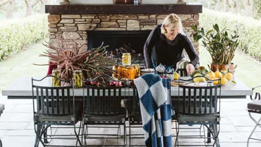 A woman setting a dining room table in front of windows to the garden