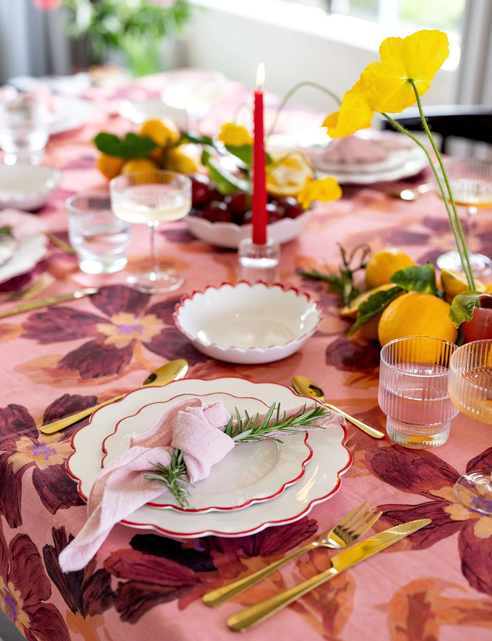 A table setting with a pink table cloth and white plates with red trimming