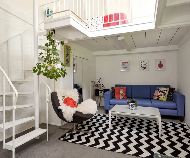 A blue couch sitting underneath an open-plan second floor with white stairs to the side