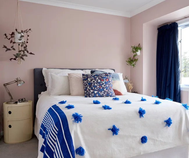 A pink-walled bedroom with a blue and white duvet cover over the double bed