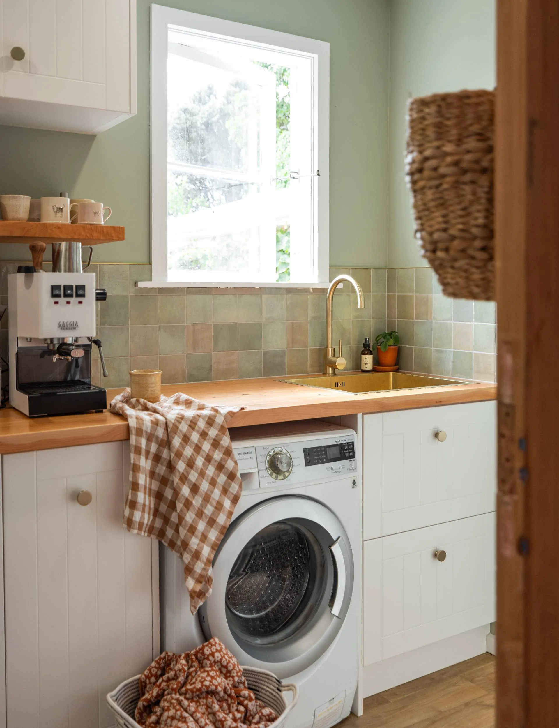 The bathroom of the Wainui Beach bungalow has green walls with green and pink tiles around the wooden bench top