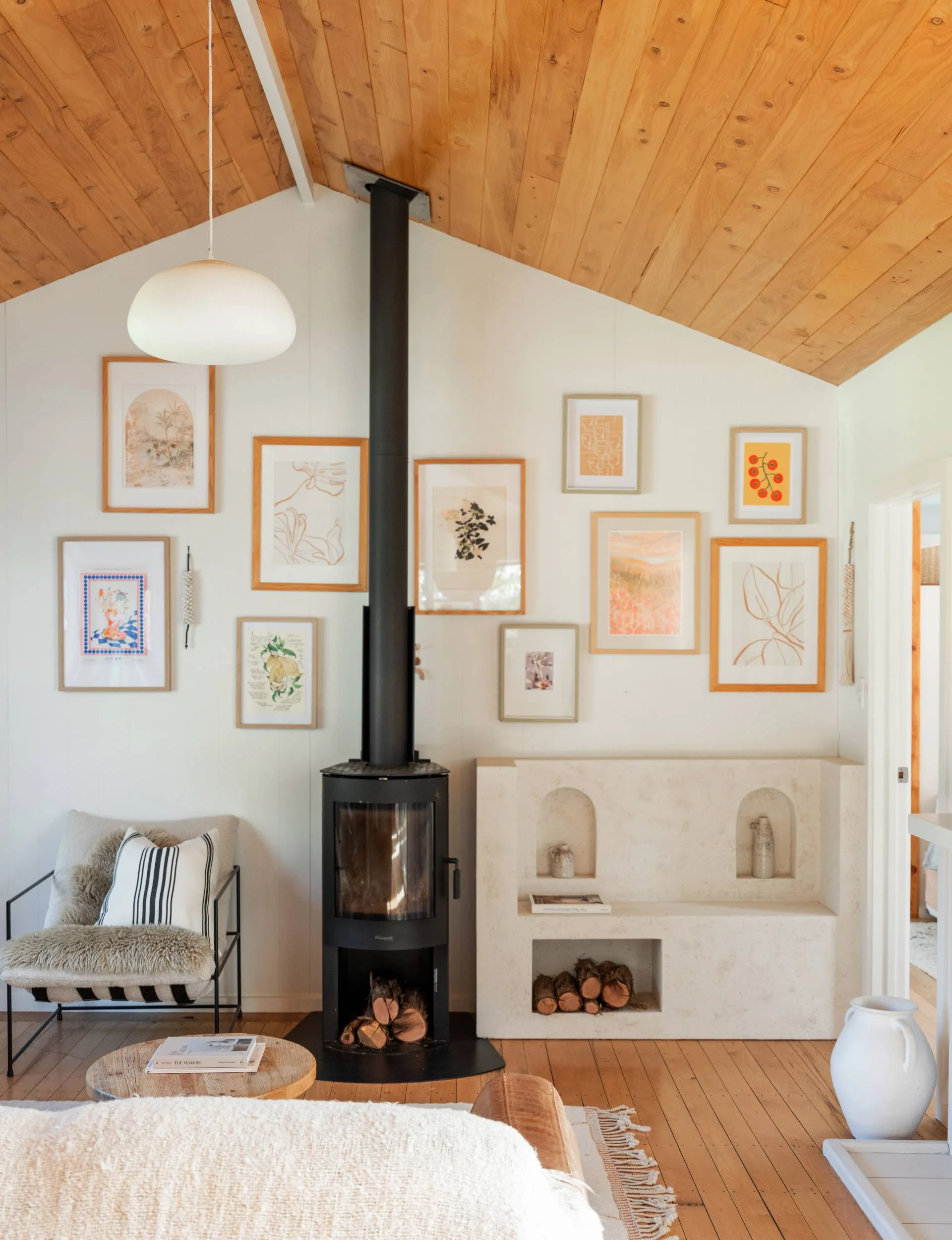 The Wainui Beach bungalow living room's A-frame roof with a tall lack fireplace in the middle of the ack wall, surrounded by a collage of photo frames