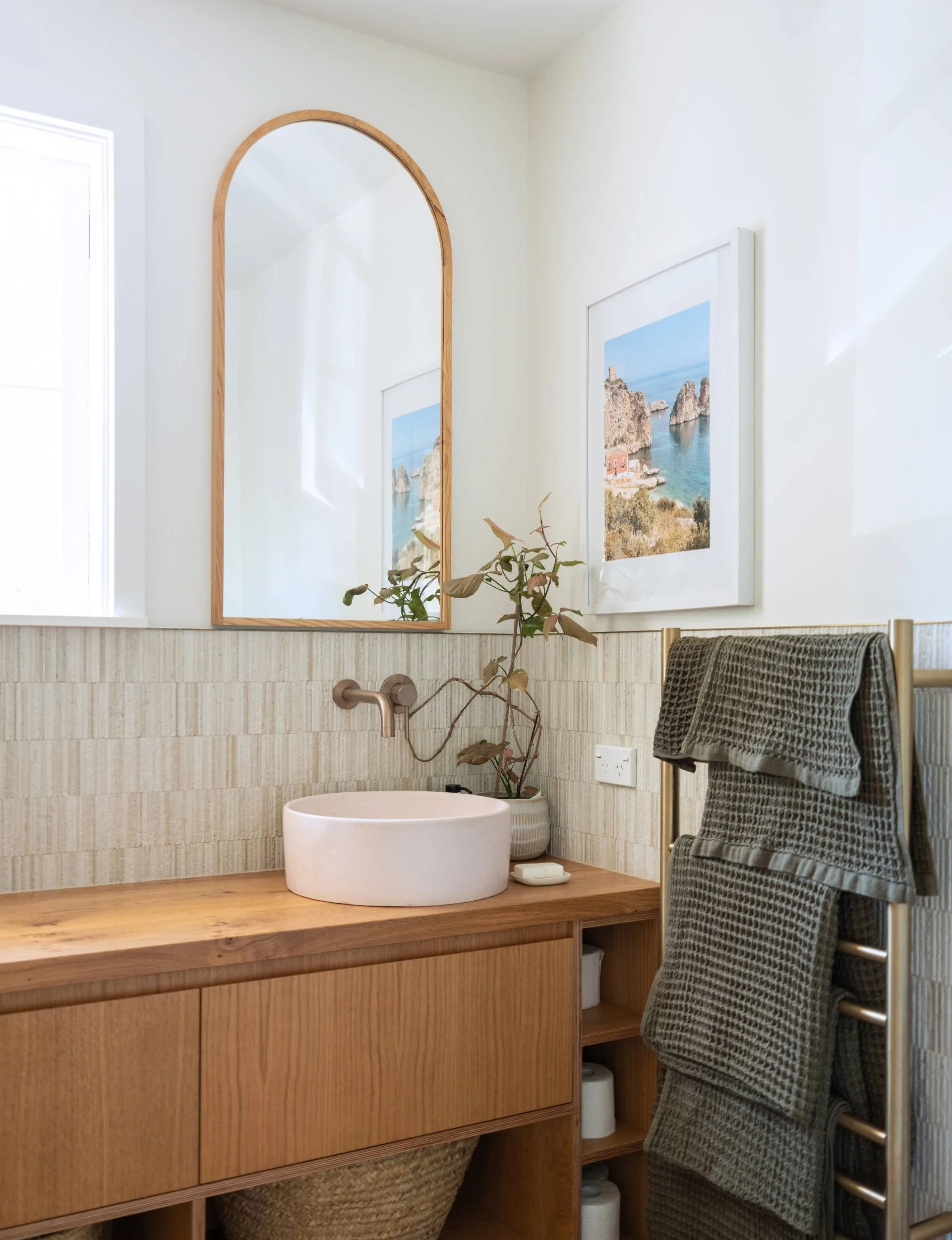 The wooden vanity in the master bathroom with a round pink sunk and an arch mirror over