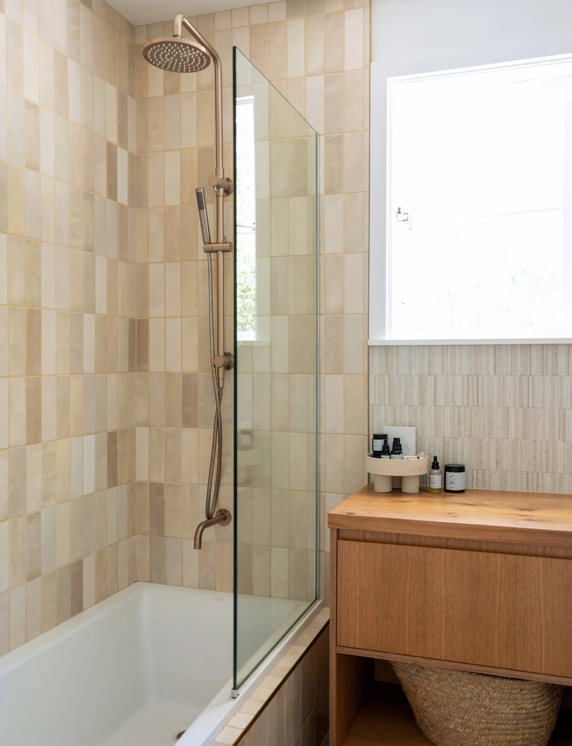 The master bathroom of the Wainui Beach bungalow with sand-coloured tiles and a wooden vanity