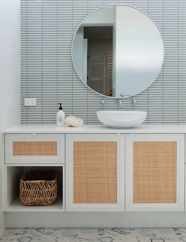 The blue-grey bathroom tiles and rattan and white vanity