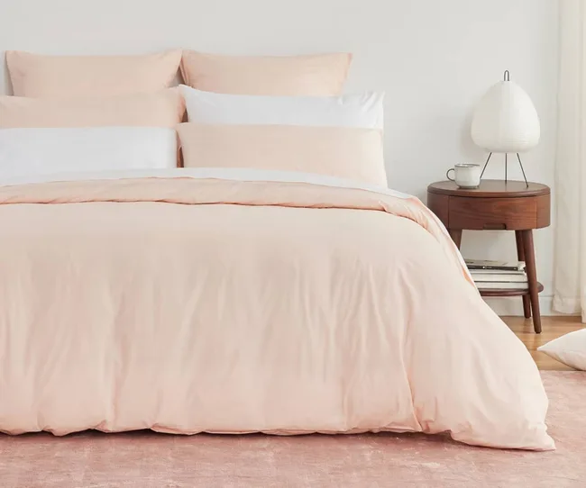 A perfectly made bed with a pink duvet cover, pink sheets and pink and white pillows
